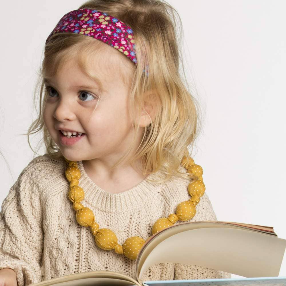 Child wearing a colorful headband and yellow necklace, holding an open book.