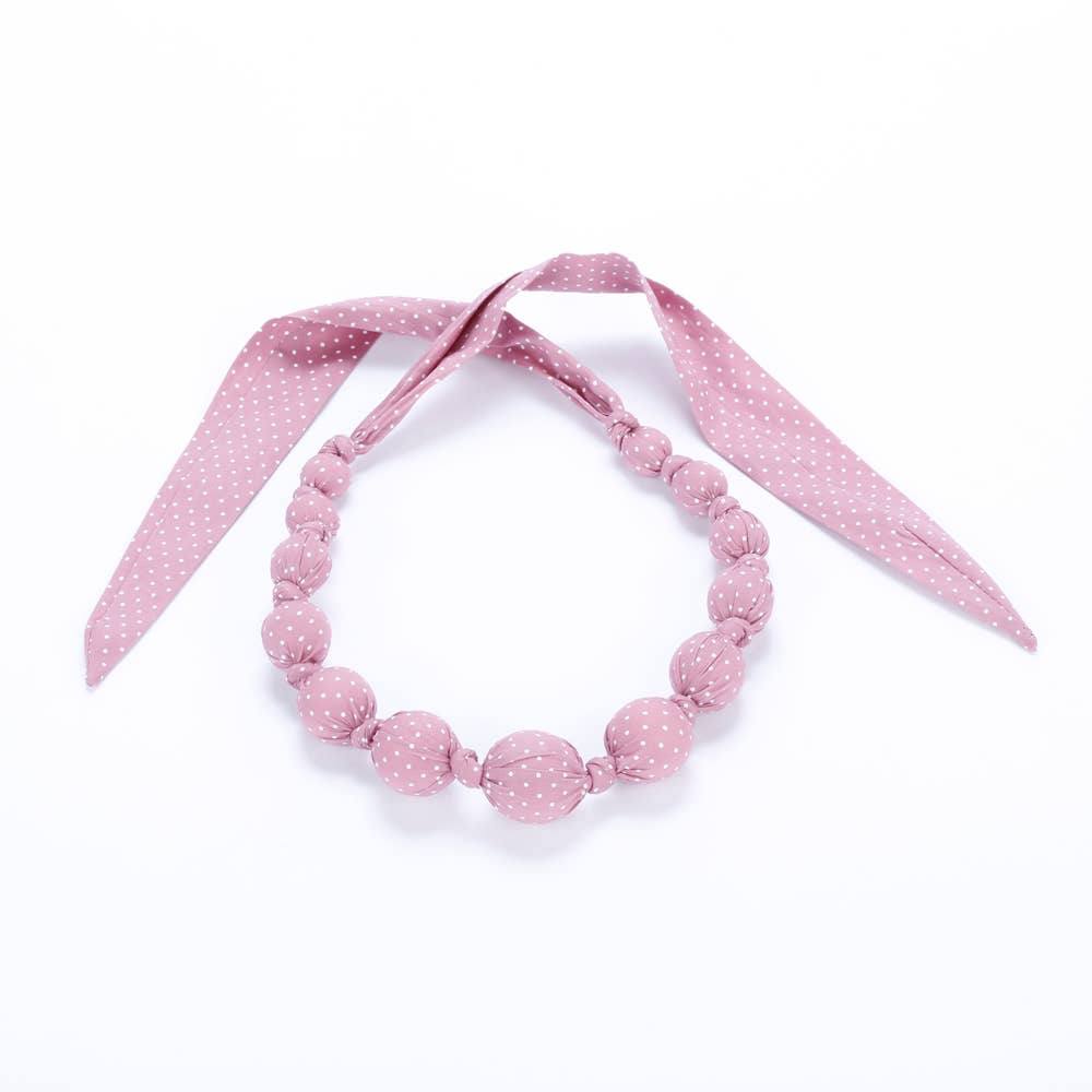 Pink polka dot necklace with matching ribbon on a white background